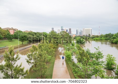 High and fast water rising in Bayou River along Allen Parkway and Memorial Drive with downtown Houston in background, storm cloud sky. Heavy rain from tropical storm cause many flood. People wandering