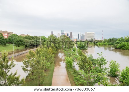 High and fast water rising in Bayou River along Allen Parkway, pathway/bike trail, Memorial Drive. Downtown Houston in background under storm cloud sky. Heavy rain from tropical storm cause many flood
