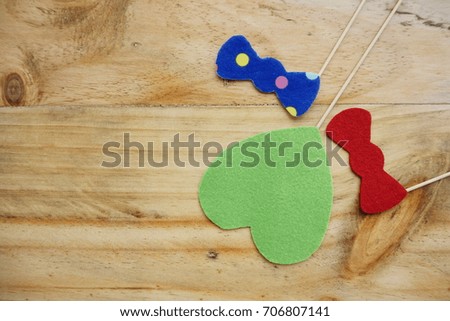 Top or flat lay view of Photo booth props a green heart shape, a red bow tie and a blue polkadot bow tie on a wooden background flat lay. Birthday parties and weddings.