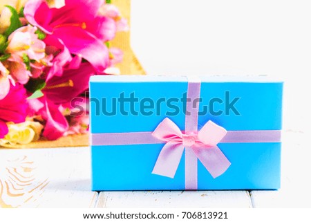Gift in a box and a bouquet of flowers on a white wooden table. Birthday party.