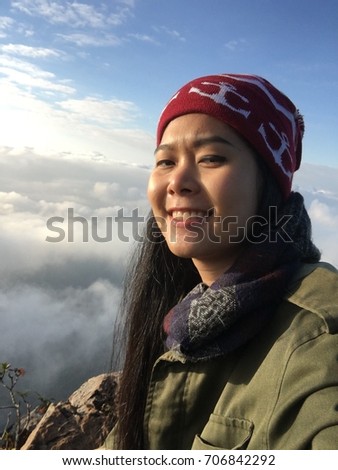 Beautiful girl standing on top of a hill and taking photos selfie with the sky and clouds as the background. Doi Luang Chiang Dao, Chiang Mai Province, Thailand.
