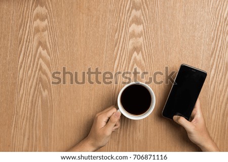 Man using smart phone sitting on table, hand holding smart phone showing screen.