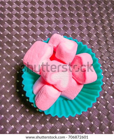 Marshmallows in heart shape put in a green cup on dish mat. 