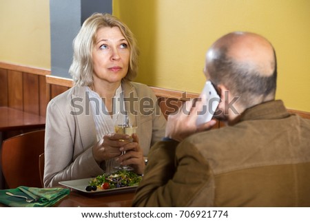 elderly blonde woman bored in a restaurant while her man talking on the phone
