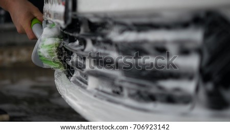 worker washes the grill of the car's radiator with a green brush, foam