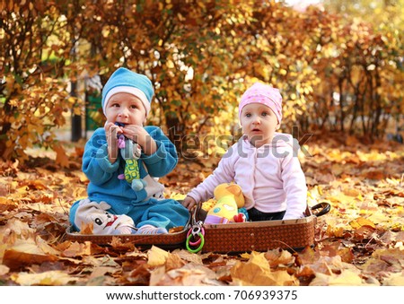Two Little child in nature sitting in open suitcase. Outings - the forest in autumn. Nearby are big hare toy