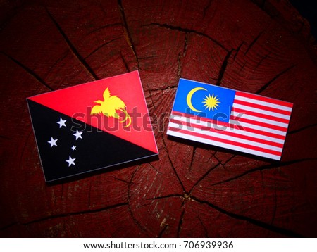 Papua New Guinea flag with Malaysian flag on a tree stump isolated