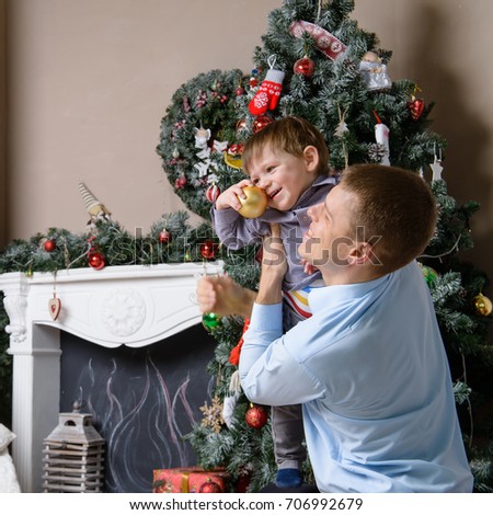 Close-up of cute caucasian dad holding a child. Little son holding a Christmas toy, on the background fireplace and decorated Christmas tree. Concept of Christmas and New Year