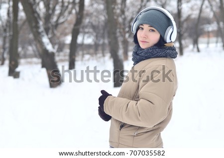 Pretty young girl wear warm winter earmuffs and scarf. Fun brunette female model walk outside with headphones in cold weather. Smiling happy model posing. Good holiday weather