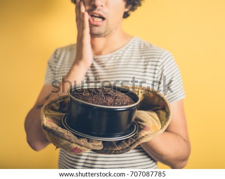 An upset young man is holding a burnt cake