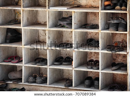 Many pairs of shoes, arranged in old, scuffed and worn cubby holes near the entrance to a Hindu temple in India.