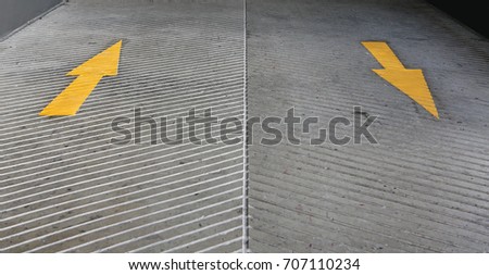 Two way Yellow Arrow signs as road markings. Arrow sign on slope floor at park building.
