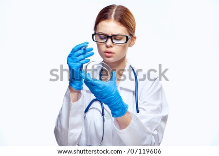 In the doctor's hand a woman in glasses a petri dish and a syringe on a light background                               