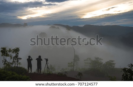 Vintage two photographers take pictures of the mountains with thick fog, golden sun, and white clouds background