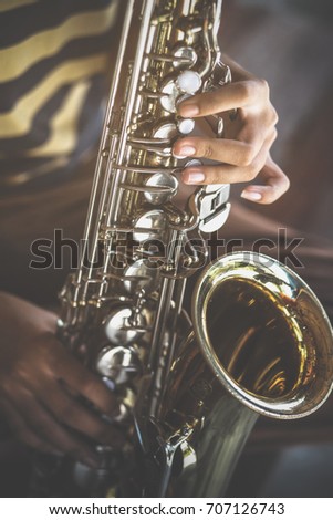 The hands of a teen musician who is blowing the saxophone.