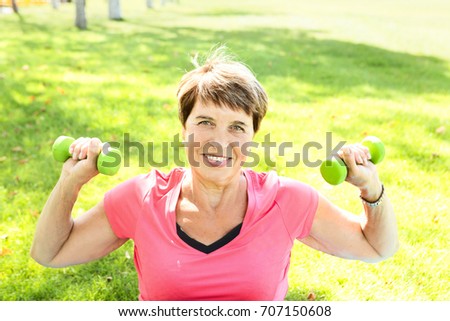 Cheerful senior lady exercising with dumbbells in the park
