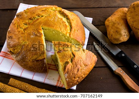 Sliced Potato Bread on wooden table with knives and potatoes.