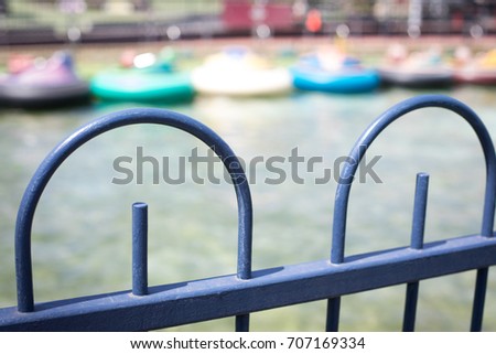 Close up of bright blue arched metal fence at a theme park separating the waiting area from bumper boat pool in background