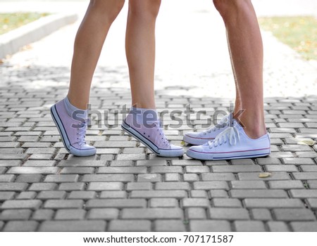 Modern urban hipster teenagers having fun. A close-up picture of teenages' legs in white and pink gumshoes on a blurred natural background. Young people kissing each other. Outdoors, romance concept.