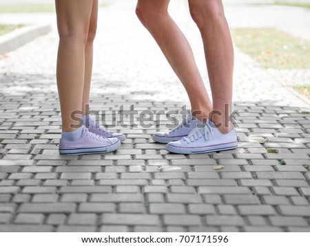 Modern urban hipster teenagers' legs. A close-up picture of teenagers' legs in white and pink gumshoes standing on a blurred cobbled background. Copy space. Outdoors, romance concept.