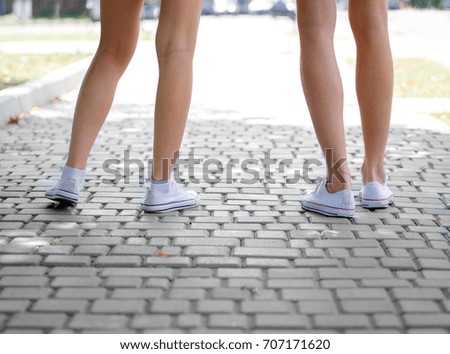  A close-up picture of teenages' legs in white and pink gumshoes standing on a blurred cobbled background. Modern urban hipster teenagers having fun. Copy space. Outdoors, romance, youth concept.