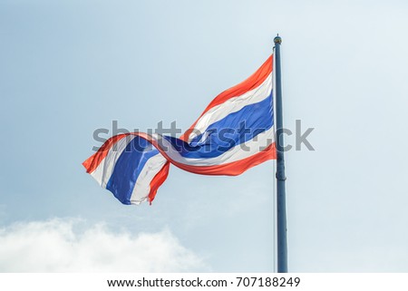 Thailand flag against a blue sky with clouds.