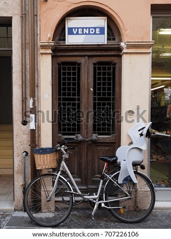 House for sale in Italy. In front of the door is parked a bicycle with child seat. "Vende" means "sells".