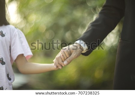 a picture of a father and daughter holding hands in the morning with the bokeh background of leaves blure