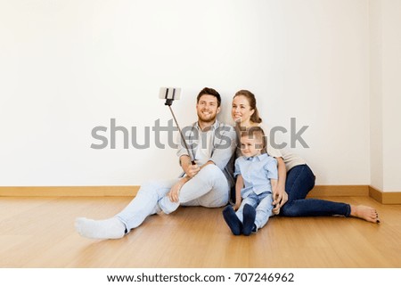 mortgage, people, housing and real estate concept - happy family with child taking picture by smartphone selfie stick at new home