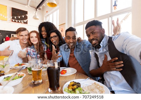 leisure, friendship, people and holidays concept - happy friends taking selfie at restaurant or bar