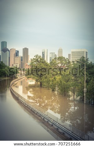 High water rising along Allen Parkway with downtown Houston in background under storm cloud sky. SUV car swamped end of s-curved road. Heavy rains from tropical storm caused many flood. Vintage tone.