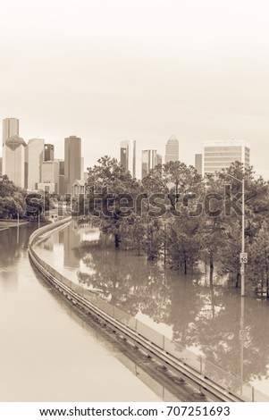 High water rising along Allen Parkway with downtown Houston in background under storm cloud sky. SUV car swamped end of s-curved road. Heavy rains from tropical storm caused many flood. Vintage tone.