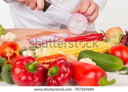 chef in white jacket slicing fresh vegetables on cutting board on white background