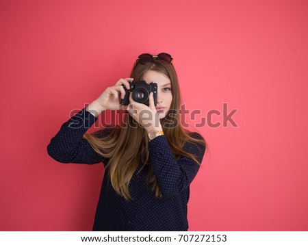 portrait of a smiling pretty girl taking photo on a retro camera isolated over red background