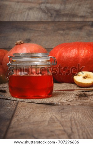 A close-up picture of a colorful autumn composition. Bright orange vegetables and cut fruits full of vitamins next to a glass jar of apple jam on a wooden background. Autumn harvest. Copy space.
