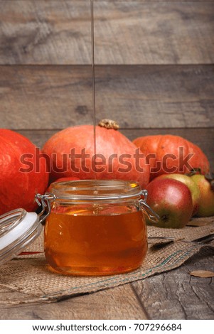 A close-up picture of bright orange vegetables and whole fruits full of vitamins next to an opened glass jar of honey on a wooden background. Pouring honey. Autumn harvest. Copy space.