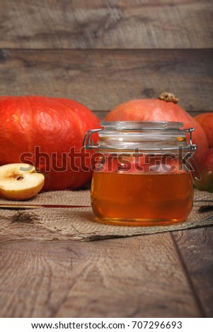 A close-up picture of a colorful autumn composition. Bright orange vegetables and cut fruits full of vitamins next to a glass jar of honey on a wooden background. Autumn harvest. Copy space.