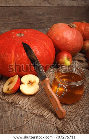 A close-up picture of a season composition. Bright autumn pumpkins and apples full of vitamins next to a glass jar of honey on a wooden table background. Autumn harvest. Copy space.
