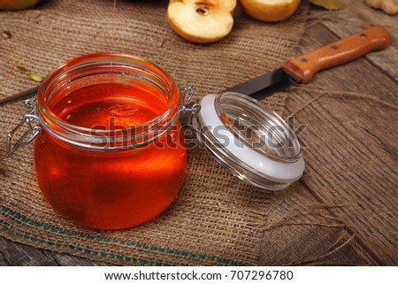  A close-up picture of a bright autumn candied fruit jelly next to orange vegetables full of vitamins and a knife on a wooden table background. Sweet honey on a rustic napkin. Autumn harvest.