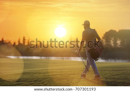 handsome middle eastern golfer carrying bag and walking to next hole at golf course on beautiful sunset in background