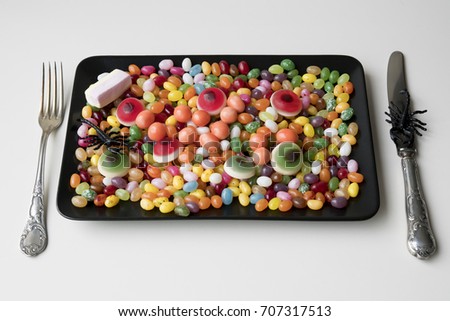 Halloween sweet meal with mixed candy, jelly beans, eyes, on black plate, with silver fork and knife