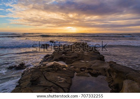 A jetty reaches out towards a sunset over the pacific ocean taken from La Jolla San Diego, California.