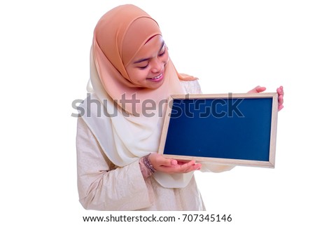 Young Asian college girl student standing isolated on white background, holding a blank chalkboard and smiling.