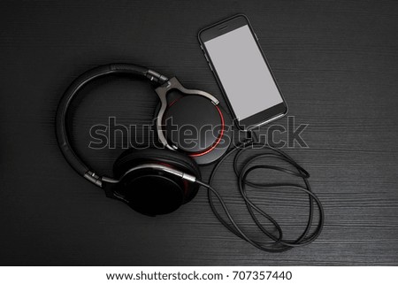 Full size Headphone connect to Mobile Phone with white background on the black wooden table.