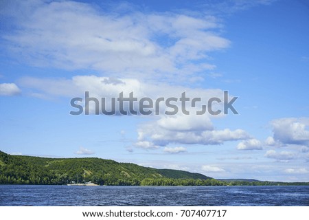River landscape in a bright sunny day with clouds. The beach with green hills and forest