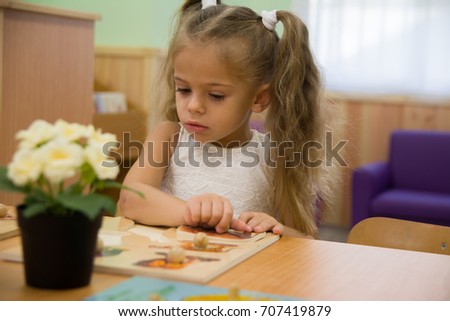 Happy little child, adorable blonde toddler girl, having fun playing with jigsaw puzzle assembling pieces of picture together sitting indoors at small white table