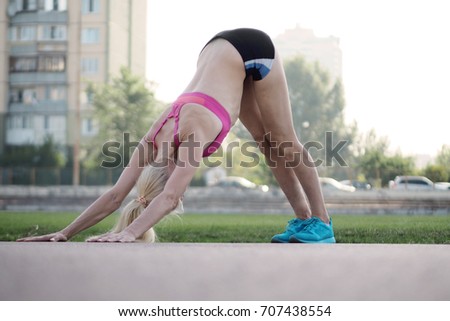 Flexible beautiful blond woman is practicing yoga and doing asana Adho Mukha Shvanasana on the stadium Royalty-Free Stock Photo #707438554