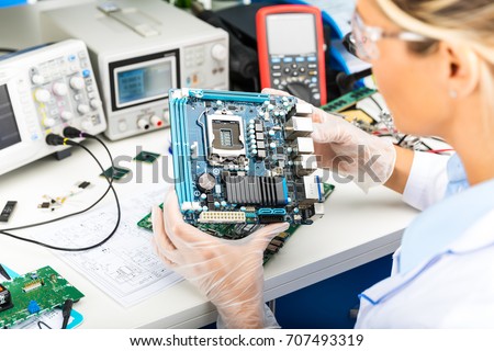 Young female digital electronic engineer examining computer PC motherboard in laboratory