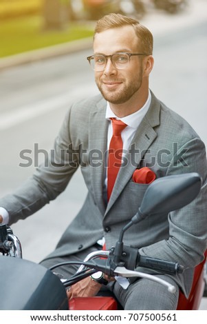 Favorite vehicle. Waist up of a positive young businessman smiling and sitting on the motorbike while going to ride