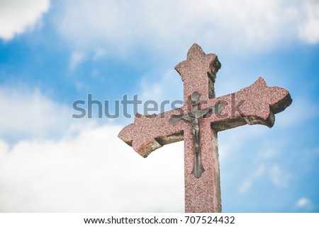 Stone cross and Jesus on the cross against a background of blue sky and clouds. Conceptual stone cross religion symbol.